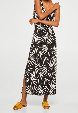 Robe maxi à motifs noir et blanc avec un décolleté en V et une fente sur le côté, confectionnée dans un tissu léger. Associée à des sandales plates jaunes.