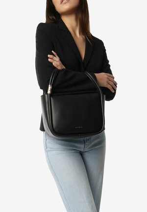 Black leather shoulder bag with a rounded shape, gold hardware accents, and a smooth texture, held by a person in a black blazer.