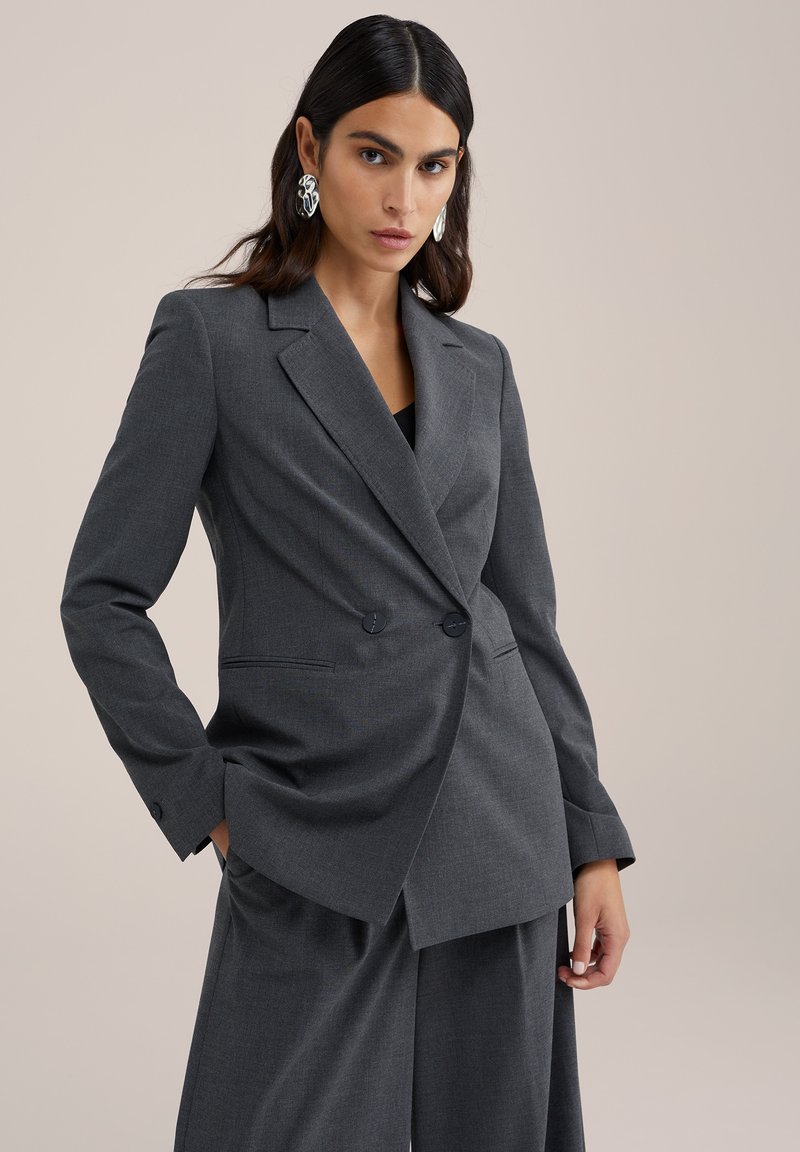 Šedý přizpůsobený blazer s dvojitým zapínáním, ostrými klopami a strukturovaným střihem. Vyrobený z texturované tkaniny s jemnými vzory.