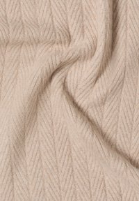 Tela texturizada de color beige claro con un patrón de espiga, que presenta una apariencia suave y acogedora, además de un brillo sutil. Adecuada para ropa o tapicería.
