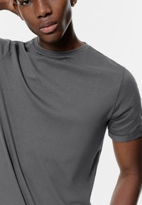 Siva kratka majica z mehkega blaga, z okroglim izrezom in zavihanimi rokavi, z gladko teksturo in oprijeto zasnovo.