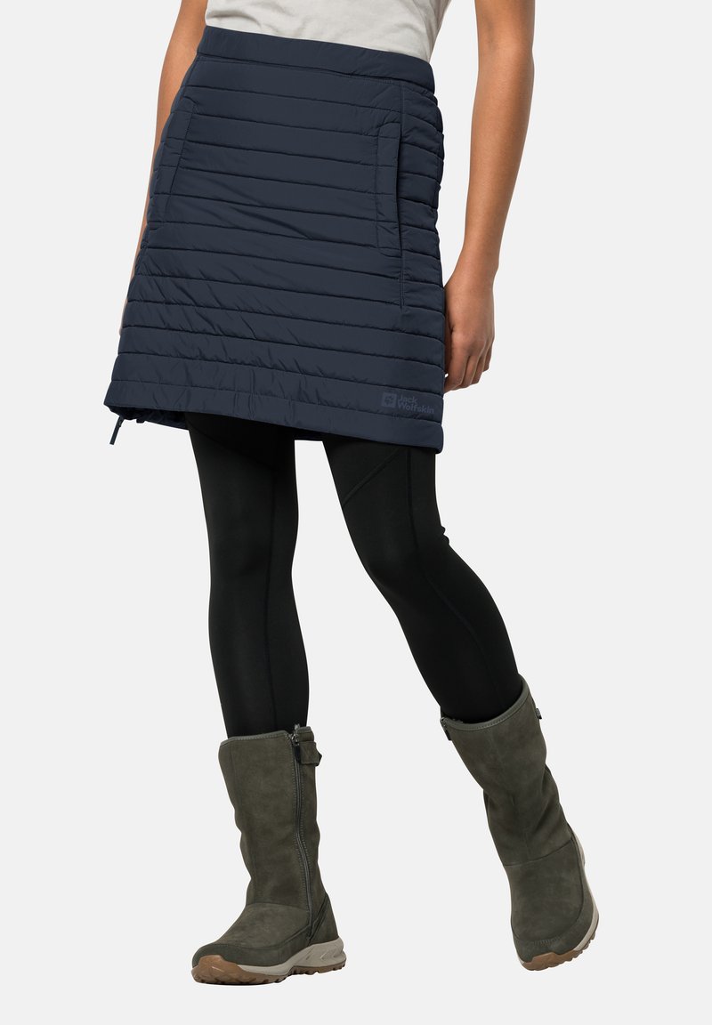 Marine blauwe gewatteerde rok met horizontaal quiltpatroon, zijzakken en een logo-label; gecombineerd met zwarte leggings en kniehoge grijze laarzen.