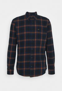 Chemise à manches longues boutonnée avec motif à carreaux bleu marine et marron et petit logo sur la poitrine gauche.