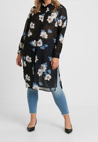 Sort blomsterbluse med lange ærmer, prydet med hvide og blå blomsterprint, semi-gennemsigtigt materiale, knaplukning foran og sideslids.