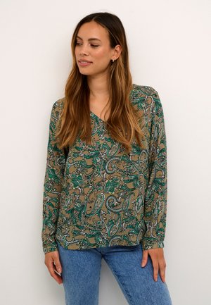 Langarmige blouse in groen en beige paisleypatroon, met een V-halsontwerp en zachte stof, gecombineerd met lichtblauwe denim jeans.