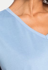 Maglietta blu chiaro a scollo a V realizzata in un tessuto morbido e liscio. Presenta un collo pulito con cuciture sottili e una texture minimale.