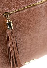 Sac à main en cuir marron texturé avec une fermeture éclair dorée et un pompon en daim assorti attaché à la tirette de la fermeture.