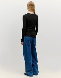 Zwarte langemouwen shirt gecombineerd met loszittende blauwe denim jeans. De jeans hebben grote achterzakken en vallen ontspannen.