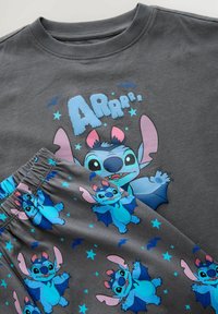 Graues Baumwoll-Schlafanzugset mit einem Cartoon-Charakter mit großen Ohren. Das Oberteil hat einen Druck mit "ARrrr" und Sternen, die Hose zeigt ein sich wiederholendes Charaktermuster.