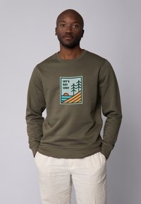 Olivegroen sweatshirt met een ronde hals, voorzien van een gedrukte graphic van bergen, bomen en een zon, aangekleed met blauwe en oranje kleuren.