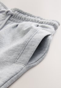 Primo piano di pantaloni della tuta grigio chiaro che mostrano la vita elastica e la tasca laterale con cuciture visibili su tessuto morbido.