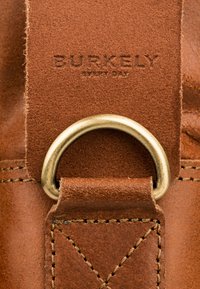 Bruine lederen band met reliëftekst "BURKELY" en "EVERY DAY", uitgerust met een gouden metalen ring en fijne steekdetails.