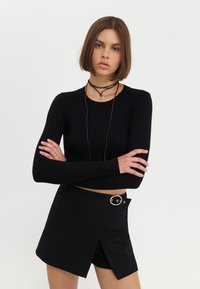 Haut court à manches longues en maille noire associé à une jupe noire avec une boucle en anneau argentée et un ourlet asymétrique.