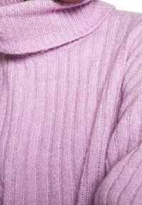 Licht paarse geribde turtleneck trui gemaakt van een zachte, gestructureerde stof. Kenmerkt zich door een brede, gevouwen kraag en losse mouwen.