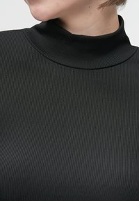Top negro de cuello alto con diseño ajustado y canalé. La tela tiene una textura suave con sutiles líneas verticales.