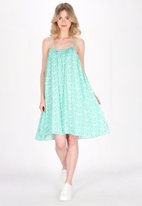 O rochie de soare verde mentă cu modele florale albe, având bretele subțiri și o croială lejeră, asortată cu adidași albi.