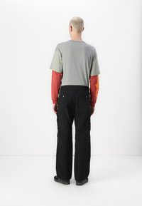 T-shirt gris à manches courtes superposé à une chemise à manches longues rouge ; associé à un pantalon cargo noir avec poches latérales et coupe décontractée.