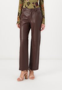 Brown faux leather wide-leg pants featuring a high waist, side pockets, and a smooth texture. Paired with light pink block-heeled sandals.