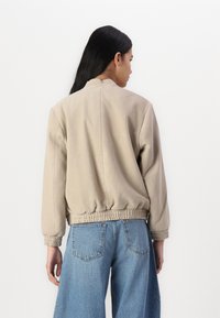 Beige bomber-jakk, millel on ümmargune kaelus, elastne vöökoht ja pikad varrukad, valmistatud pehmest nahkjasest materjalist.