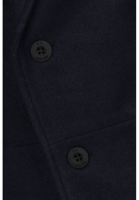 Tissu bleu marine foncé avec deux boutons noirs à quatre trous cousus sur une couture, montrant les détails de texture et de couture en gros plan.