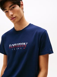 Tumši zils kokvilnas T krekls ar balto un sarkano "tommy" logos, apaļu kakla izgriezumu, īsām piedurknēm un mazu logotipu akcentu uz apakšmalas.