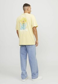 T-shirt di cotone gialla con una grafica colorata di un fiore di cactus sul retro, abbinata a jeans azzurri a vestibilità comoda e sneaker bianche.