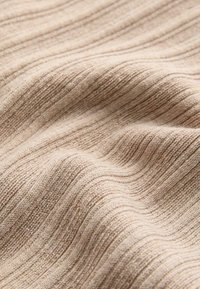 Beżowa prążkowana dzianina z miękką, fakturowaną powierzchnią, ukazująca zakrzywione fałdy i drobne detale szwów.