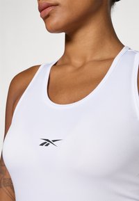 Tricou sport alb fără mâneci, cu guler rotund, având un mic logo Reebok negru pe piept. Material neted, cu un design ajustat.