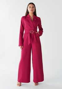 Fuksija kombinezon z oblikovano zasnovo, dolgimi rokavi in širokimi hlačnicami, z pasom in ovratnikom z režo.