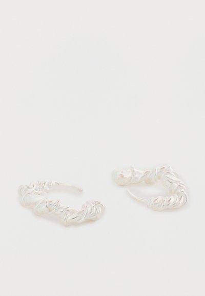 Cercei din argint în formă de cerc răsucit cu design texturat. Bucllele au forme neregulate, oferind un aspect unic și contemporan.