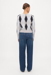 Πλεκτό πουλόβερ σε ανοιχτό γκρι χρώμα με σχέδιο αργκάλι σε ναυτικό μπλε και ανοιχτό μπλε. Συνδυάζεται με φαρδιά τζιν ψηλόμεσα σε σκούρο μπλε χρώμα.