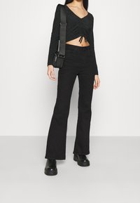 Mustat, lyhytvartiset pitkät hihat -paita, jossa on kootut etuosan yksityiskohdat. Yhdistetty mustiin leveälahkeisiin farkkuihin ja paksupohjaisiin mustiin saappaisiin.