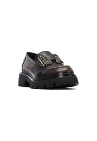 Zapato de cuero negro con una suela gruesa, que presenta una correa prominente adornada con tachuelas y acentos metálicos. Textura suave y forma redondeada.