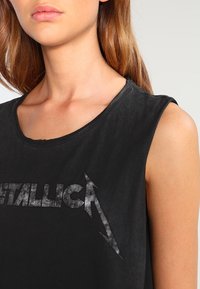 Mustapaitainen hihaton T-paita, joka on valmistettu puuvillasta. Edessä on haalistunut "Metallica" -graafiikka ja salaman muotoinen kuvio. Sujuva pinta.
