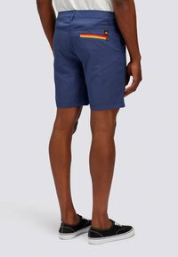 Pantaloni corti blu navy con una tasca posteriore dotata di una zip multicolore. Tessuto liscio con una vestibilità regolare. Indossati con scarpe da ginnastica nere.