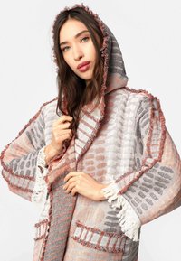 Kapucňový cardigan s třásněmi na okrajích, s šedým a korálovým vzorem. Vyrobeno z lehké tkaniny, s předními kapsami a volnými rukávy.