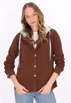 Bruine corduroy jas met een grijze capuchon, met twee voorzakken en knoopsluiting. Draagt over een witte shirt. Casual pasvorm.