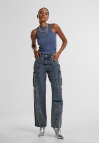 Tank top in blue, paired with high-waisted, loose-fitting denim cargo pants featuring front pockets and side panels. Metallic silver heels.