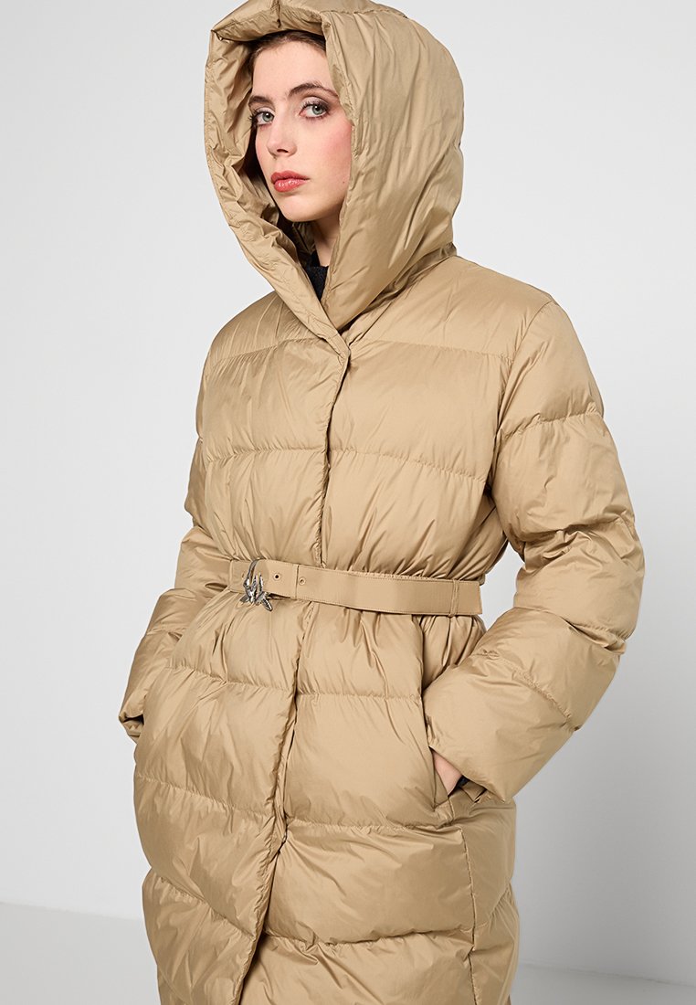 Cappotto imbottito beige con cappuccio, caratterizzato da una vita con cintura. Tessuto strutturato e trapuntato con vestibilità comoda e ampie tasche anteriori.