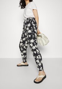 Pantalones con un patrón de hojas de palma en blanco y negro, con una cintura elástica, corte ajustado y combinados con sandalias planas de color claro.