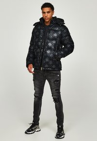 Black puffer jacket with a glossy finish, featuring an embossed pattern. Worn with distressed black jeans and chunky black sneakers.