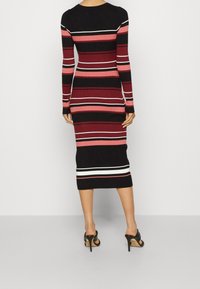 Robe à manches longues côtelée avec des rayures verticales noires, bordeaux et roses, agrémentée d'accents blancs près de l'ourlet. Silhouette ajustée, longueur mi-mollet.