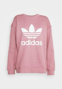 Sweatshirt rose fait d'un tissu à texture douce, arborant un grand logo Adidas blanc et trois bandes au-dessus du logo sur le devant.