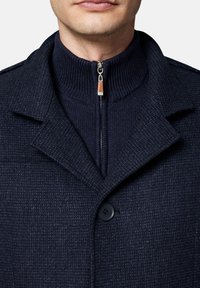Granatowy płaszcz z wełny z domieszką, charakteryzujący się teksturowanym materiałem, zapięciem na guziki oraz wysokim kołnierzem z zamkiem błyskawicznym w dopasowanej kolorystyce.