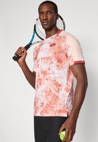 Camiseta atlética de manga curta, em rosa claro e padrão abstrato vermelho, feita de um tecido respirável, com decote redondo e fendas laterais para maior mobilidade.