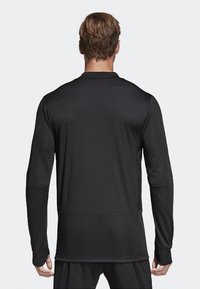 Top deportivo negro de manga larga con un diseño elegante, textura suave y un dobladillo redondeado, con sutiles detalles de costura a lo largo de las mangas.