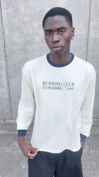 Pikaäärega kreemjas särk, millel on tumesinised aktsendid, sisaldab tumeda sinise värviga teksti "RUNNING CLUB", pehme tekstuur, mugav lõige ja ümmargune kaelaauk.