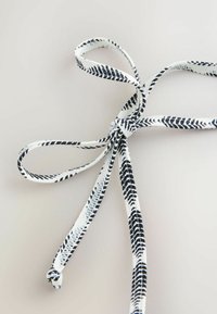 Valge lind musta triibumustriga, seotud lipsuks. Tekstuuriga materjalil on keerukad detailid mööda servasid.