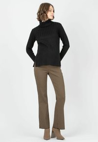 Schwarzer gerippter Rollkragenpullover kombiniert mit braunen gemusterten Schlaghosen und beigen hochhackigen Stiefeletten.