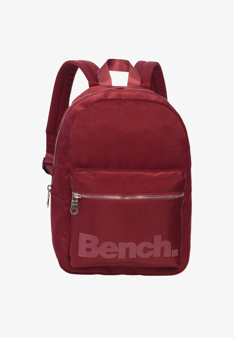 Rode stoffen rugzak met een ronde vorm, voorzien van een geaccentueerde voorzak met rits en het woord "Bench." in een lichtere tint op de onderste sectie.